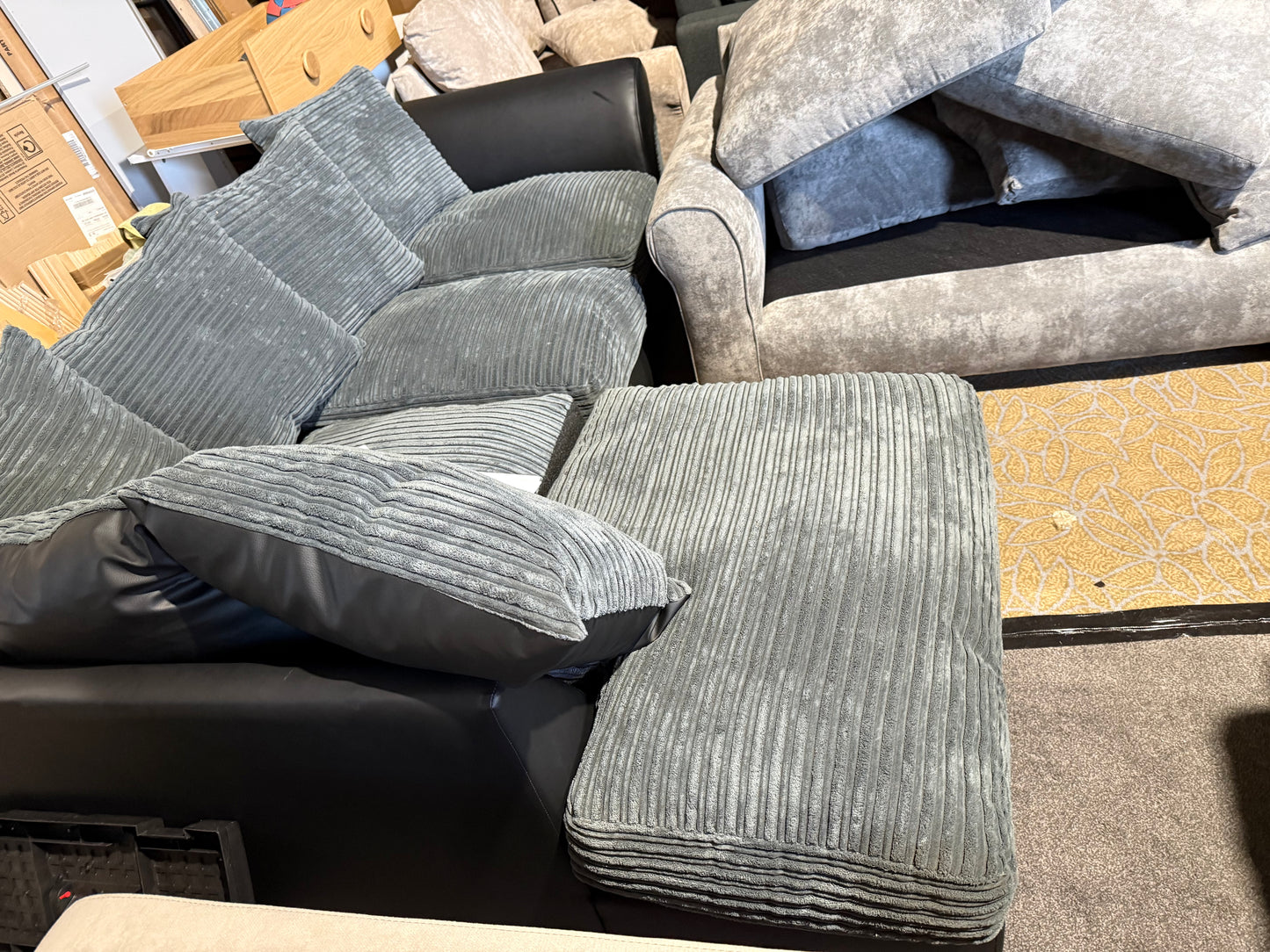 Gray upholstered furniture set on a warehouse floor with cardboard boxes in the background.